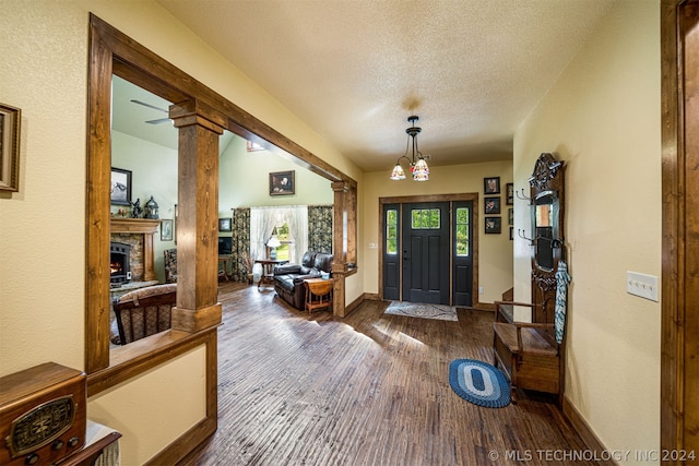 entrance foyer with a stone fireplace, a textured ceiling, dark hardwood / wood-style floors, and ornate columns