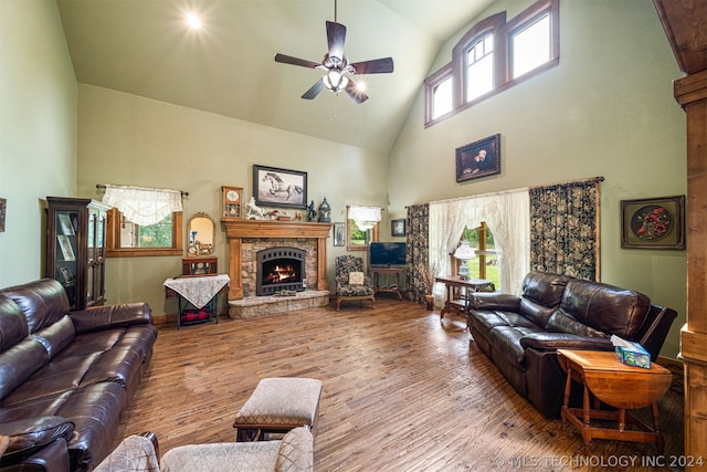 living room with a stone fireplace, a high ceiling, ceiling fan, and hardwood / wood-style floors