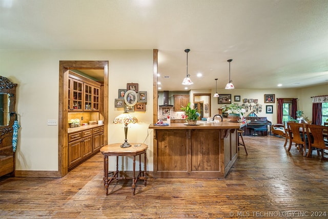 kitchen featuring wall chimney range hood, hanging light fixtures, a breakfast bar area, hardwood / wood-style floors, and sink