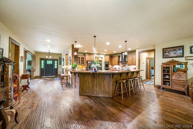 kitchen featuring decorative light fixtures, wall chimney range hood, dark hardwood / wood-style flooring, stainless steel appliances, and a kitchen breakfast bar