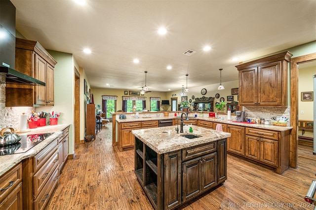 kitchen featuring a kitchen island with sink, wall chimney exhaust hood, backsplash, wood-type flooring, and sink