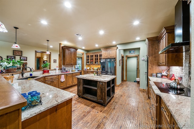 kitchen featuring wall chimney range hood, an island with sink, hardwood / wood-style flooring, high end refrigerator, and sink