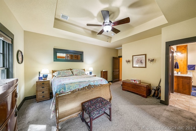 carpeted bedroom featuring ceiling fan, a tray ceiling, a textured ceiling, and connected bathroom