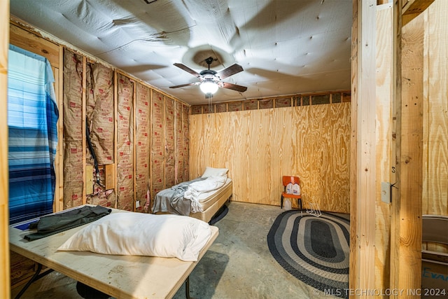 bedroom featuring wooden walls, ceiling fan, and concrete floors