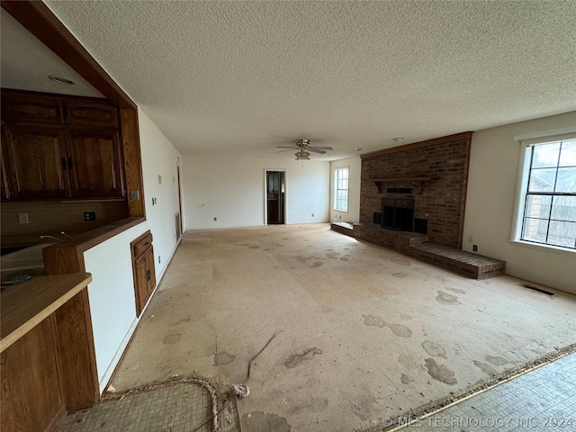 unfurnished living room featuring ceiling fan, a textured ceiling, and a brick fireplace