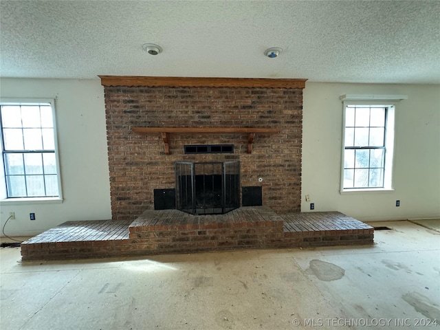 unfurnished living room featuring a textured ceiling, a fireplace, a wealth of natural light, and brick wall