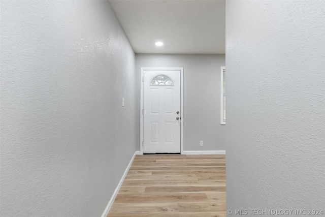 doorway with light wood-type flooring, baseboards, and a textured wall