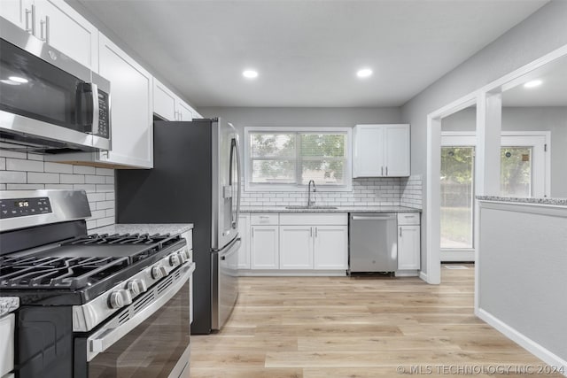 kitchen featuring light wood finished floors, appliances with stainless steel finishes, a sink, and white cabinets