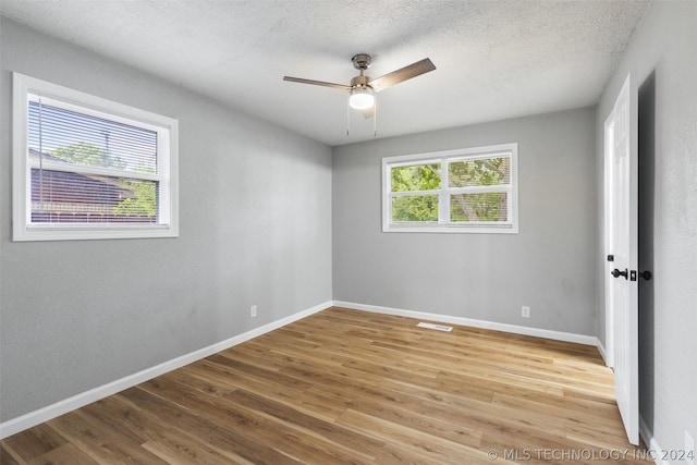 spare room with a textured ceiling, light wood finished floors, and baseboards