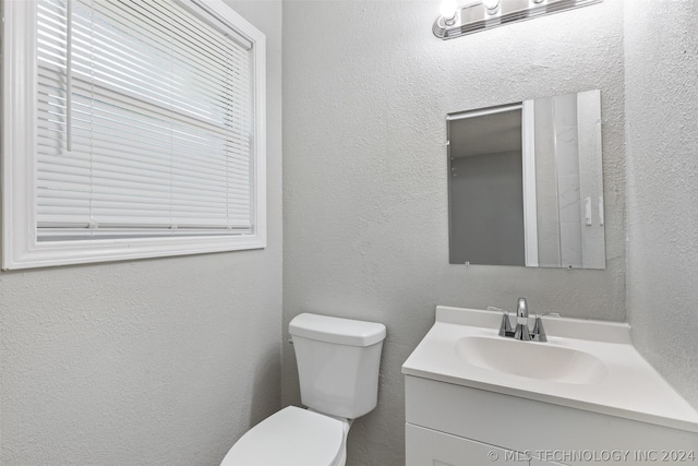 half bathroom with a textured wall, vanity, and toilet