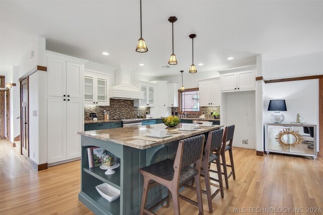 kitchen featuring white cabinets, hanging light fixtures, light stone counters, premium range hood, and a center island