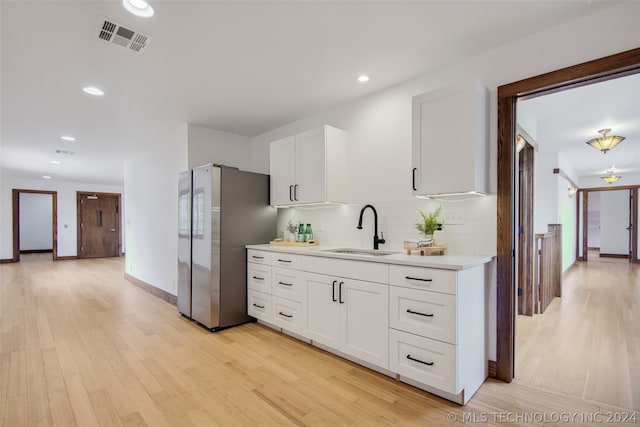 kitchen featuring sink, backsplash, stainless steel fridge, white cabinets, and light hardwood / wood-style flooring