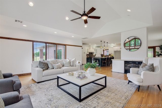 living room with a fireplace, high vaulted ceiling, light hardwood / wood-style floors, and ceiling fan