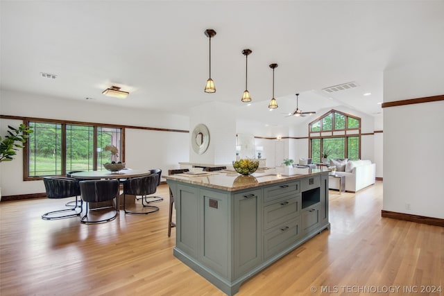 kitchen with light hardwood / wood-style floors, decorative light fixtures, light stone counters, and gray cabinetry