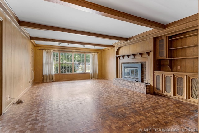 unfurnished living room with parquet floors, built in shelves, beamed ceiling, a fireplace, and wood walls