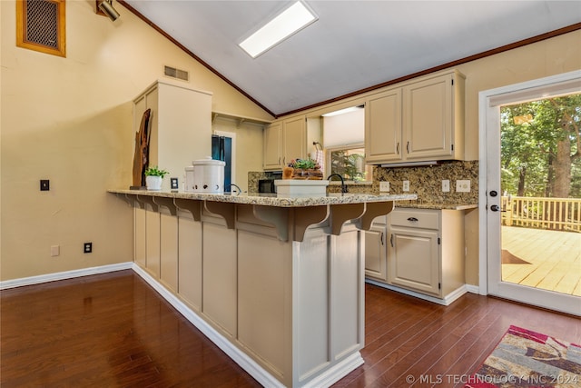 kitchen featuring light stone counters, vaulted ceiling, kitchen peninsula, and dark wood-type flooring