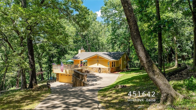 view of front of home with concrete driveway, a forest view, stone siding, a chimney, and stucco siding