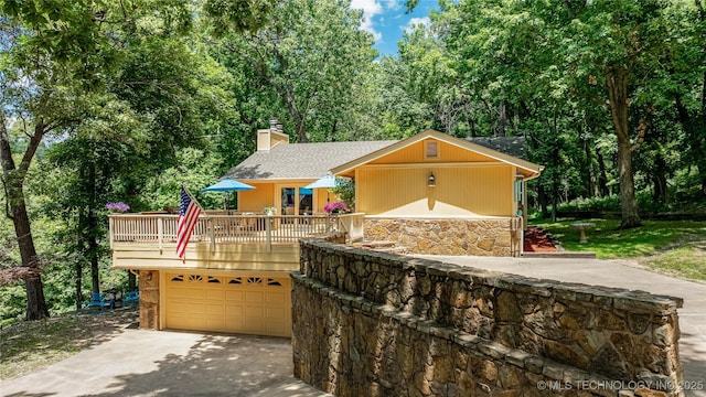 ranch-style house featuring a garage, concrete driveway, stone siding, a chimney, and a wooden deck