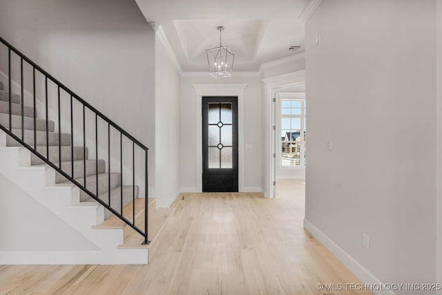 foyer with an inviting chandelier, crown molding, light hardwood / wood-style flooring, and a raised ceiling