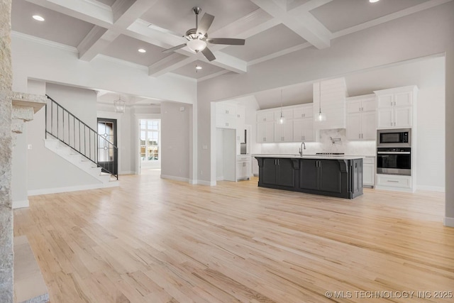 kitchen with built in microwave, light hardwood / wood-style flooring, oven, a kitchen island with sink, and white cabinets