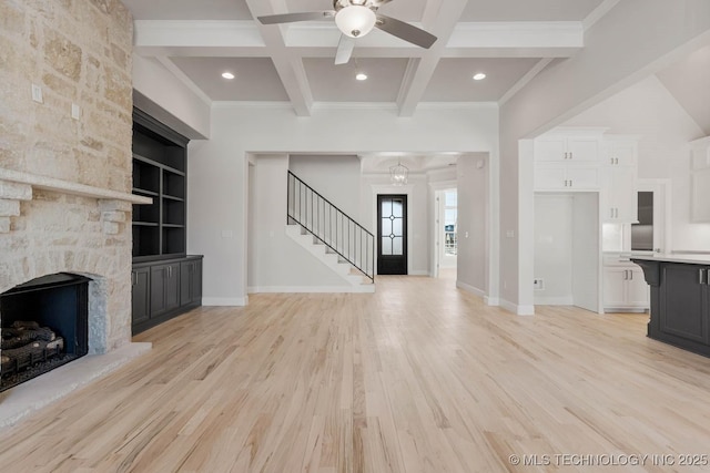 unfurnished living room featuring beam ceiling, a stone fireplace, coffered ceiling, and light wood-type flooring