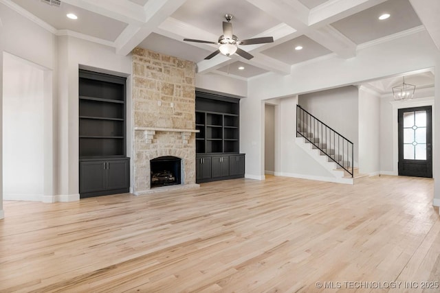 unfurnished living room with a stone fireplace, built in features, beamed ceiling, coffered ceiling, and light hardwood / wood-style flooring