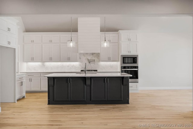 kitchen featuring built in microwave, white cabinets, oven, hanging light fixtures, and a center island with sink