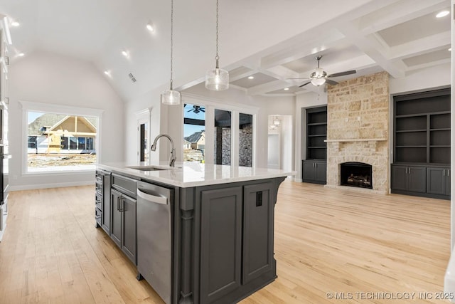 kitchen with sink, a stone fireplace, an island with sink, decorative light fixtures, and stainless steel dishwasher