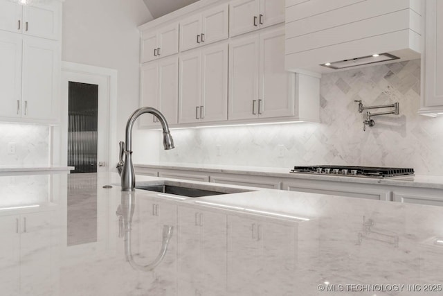 kitchen featuring sink, custom range hood, light stone countertops, decorative backsplash, and white cabinets