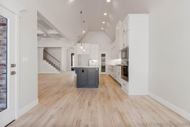 kitchen with decorative light fixtures, sink, white cabinets, a kitchen breakfast bar, and a kitchen island with sink