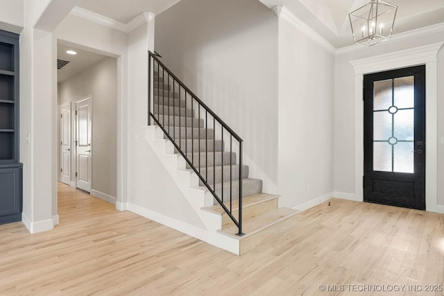 foyer entrance with ornamental molding, a notable chandelier, and light hardwood / wood-style flooring