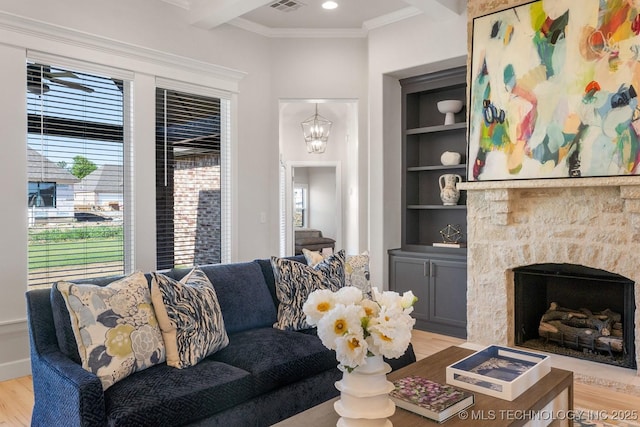living area featuring a fireplace, built in features, light wood-type flooring, beamed ceiling, and ornamental molding