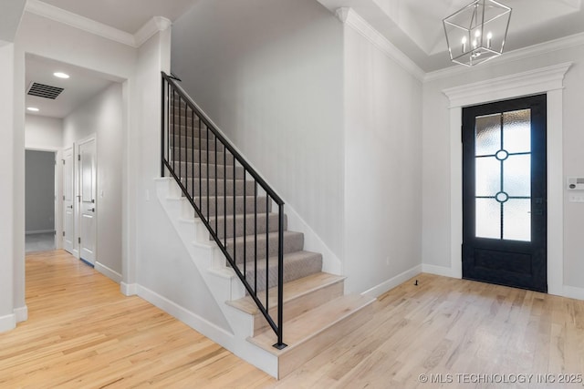 foyer entrance featuring ornamental molding, wood finished floors, a notable chandelier, and stairway