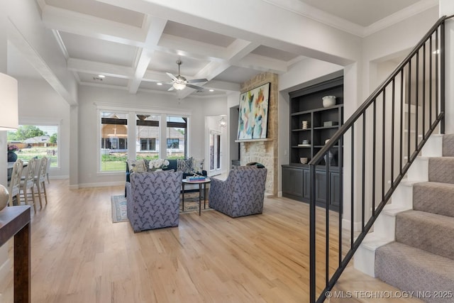 living area with a ceiling fan, baseboards, beamed ceiling, stairs, and light wood-style flooring