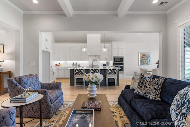 living room with ornamental molding, beamed ceiling, light wood finished floors, and visible vents