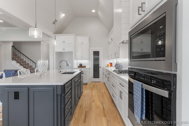 kitchen with light wood-style floors, white cabinets, a sink, decorative light fixtures, and stainless steel appliances