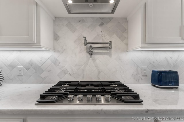 room details featuring stainless steel gas cooktop, light stone countertops, decorative backsplash, and white cabinets