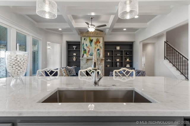 kitchen featuring ceiling fan, light stone counters, a sink, and coffered ceiling
