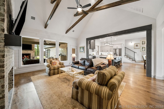 living room featuring light hardwood / wood-style flooring, a fireplace, ceiling fan with notable chandelier, beam ceiling, and high vaulted ceiling