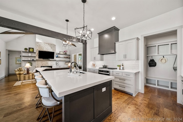 kitchen featuring an island with sink, lofted ceiling with beams, wood-type flooring, and a breakfast bar