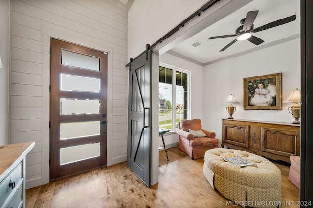 foyer entrance featuring ceiling fan, a barn door, and light hardwood / wood-style flooring