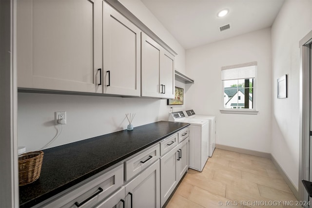 clothes washing area featuring separate washer and dryer, light tile floors, and cabinets