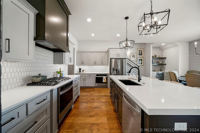 kitchen with an island with sink, backsplash, sink, hardwood / wood-style flooring, and appliances with stainless steel finishes