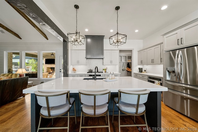 kitchen with stainless steel fridge, hardwood / wood-style floors, a center island with sink, custom range hood, and backsplash