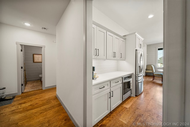 interior space featuring hardwood / wood-style floors, backsplash, white cabinetry, and appliances with stainless steel finishes