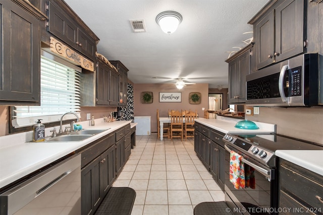 kitchen with stainless steel appliances, dark brown cabinets, light tile patterned floors, sink, and ceiling fan