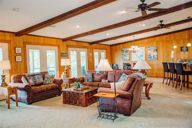 carpeted living room featuring ceiling fan with notable chandelier, vaulted ceiling with beams, french doors, and wooden walls