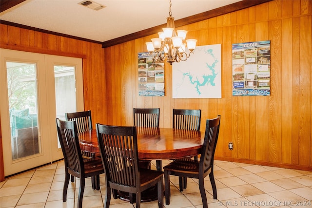 dining space featuring light tile patterned flooring, crown molding, wooden walls, and a chandelier