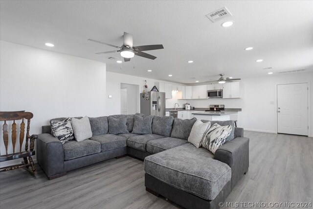 living room featuring recessed lighting, visible vents, a textured ceiling, and light wood finished floors