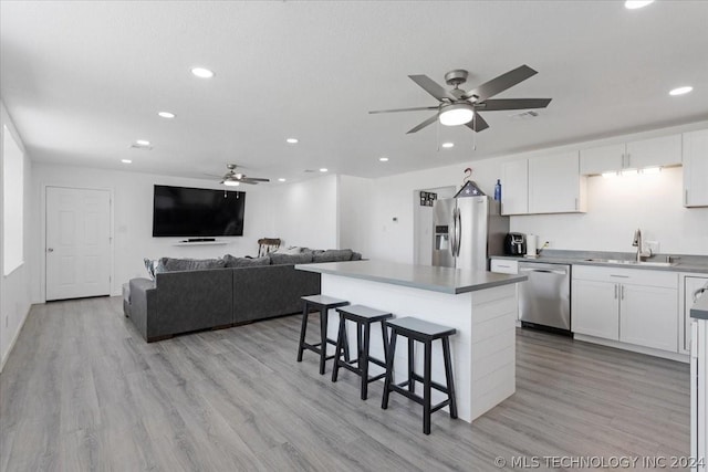kitchen featuring a breakfast bar area, a ceiling fan, a sink, stainless steel appliances, and white cabinets